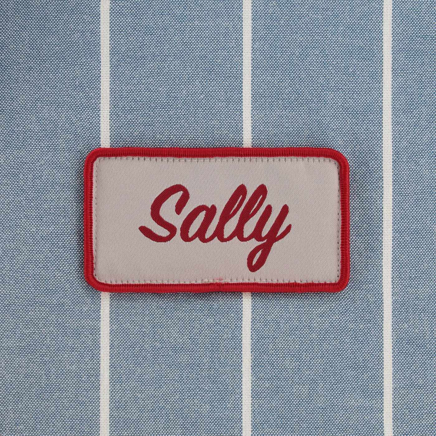 Patch with 'Sally' text on a blue striped fabric background
