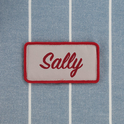 Patch with 'Sally' text on a blue striped fabric background