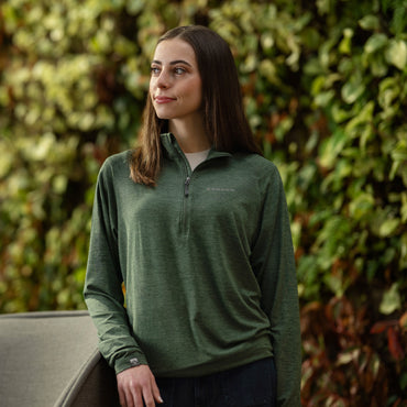 women in a green Bronco quarter zip against a greenery background