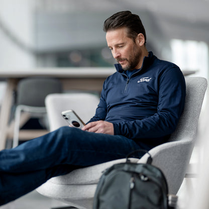 Man in a blue Ford jacket using a phone in a modern indoor setting