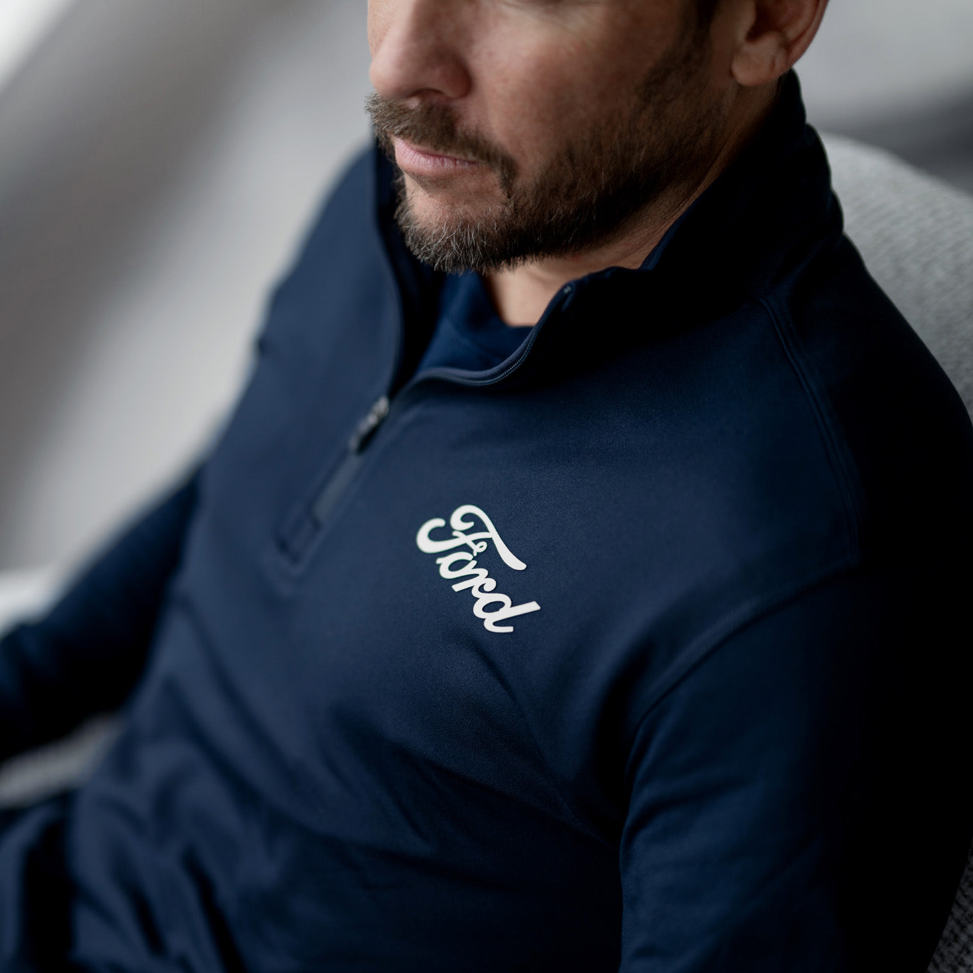 Man wearing a navy blue jacket with 'Ford' logo, sitting in a chair
