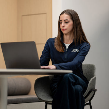 Person wearing a Ford jacket using a laptop in an office setting