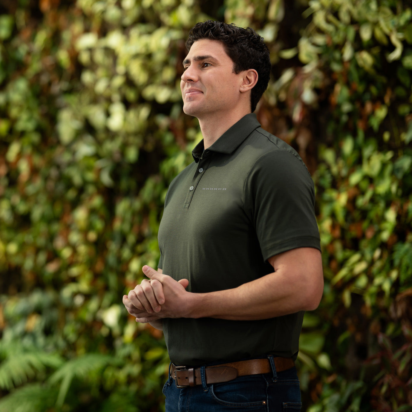Man wearing a green polo shirt standing in front of a green leafy background