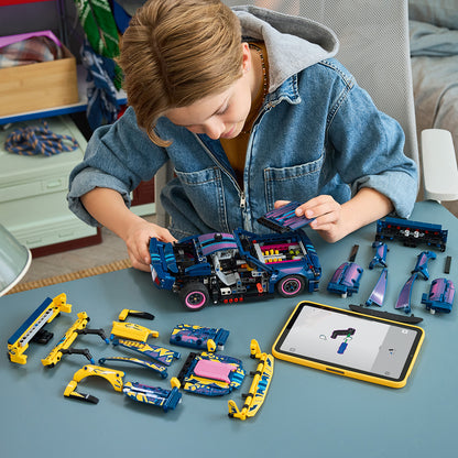 Child playing with a toy vehicle set on a table, using a tablet.