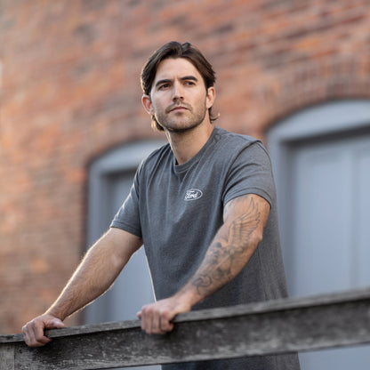 man holding onto a rail wearing a gray Ford oval t-shirt on a brick background