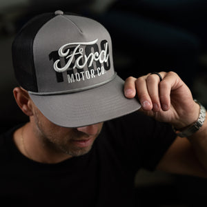 man with a watch wearing a gray hat with Ford motor co and 1903 script 