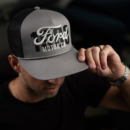 man with a watch wearing a gray hat with Ford motor co and 1903 script 