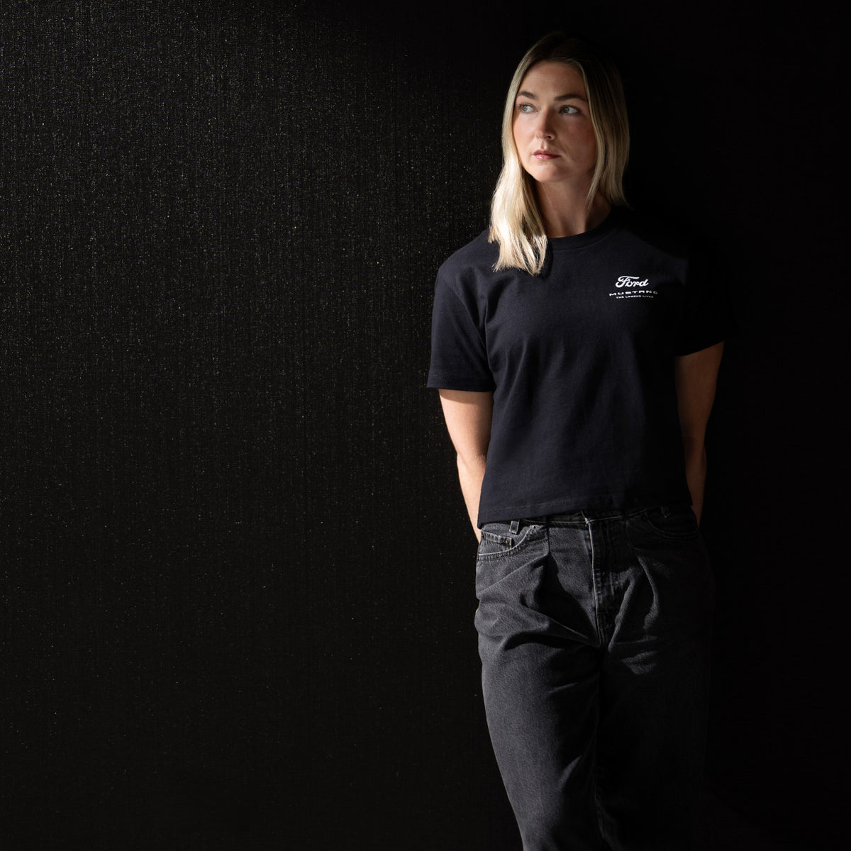woman wearing a black Ford Mustang t-shirt in black jeans and a black background
