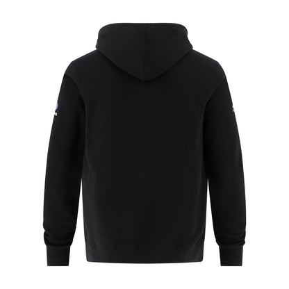 A black hooded sweatshirt shown from the back, featuring a small blue and white logo on the left sleeve, set against a plain white background.