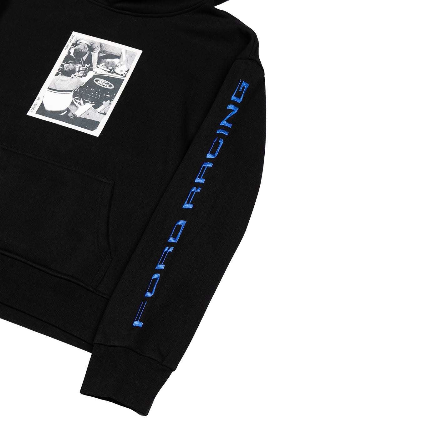 A close-up of a black hoodie featuring a vertical blue 'FORD RACING' logo printed down the right sleeve and a rectangular black-and-white graphic patch on the left chest, shown on a plain white background.