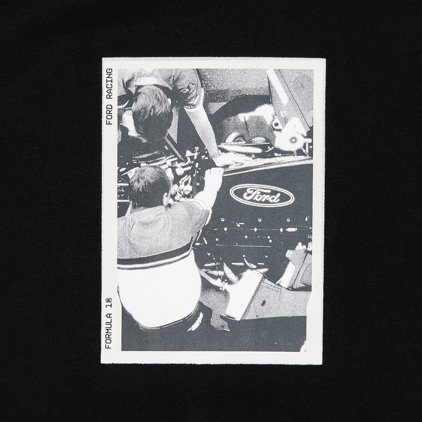 A vintage black and white Ford racing collectible card featuring drivers working on a race car, displayed against a solid black background.