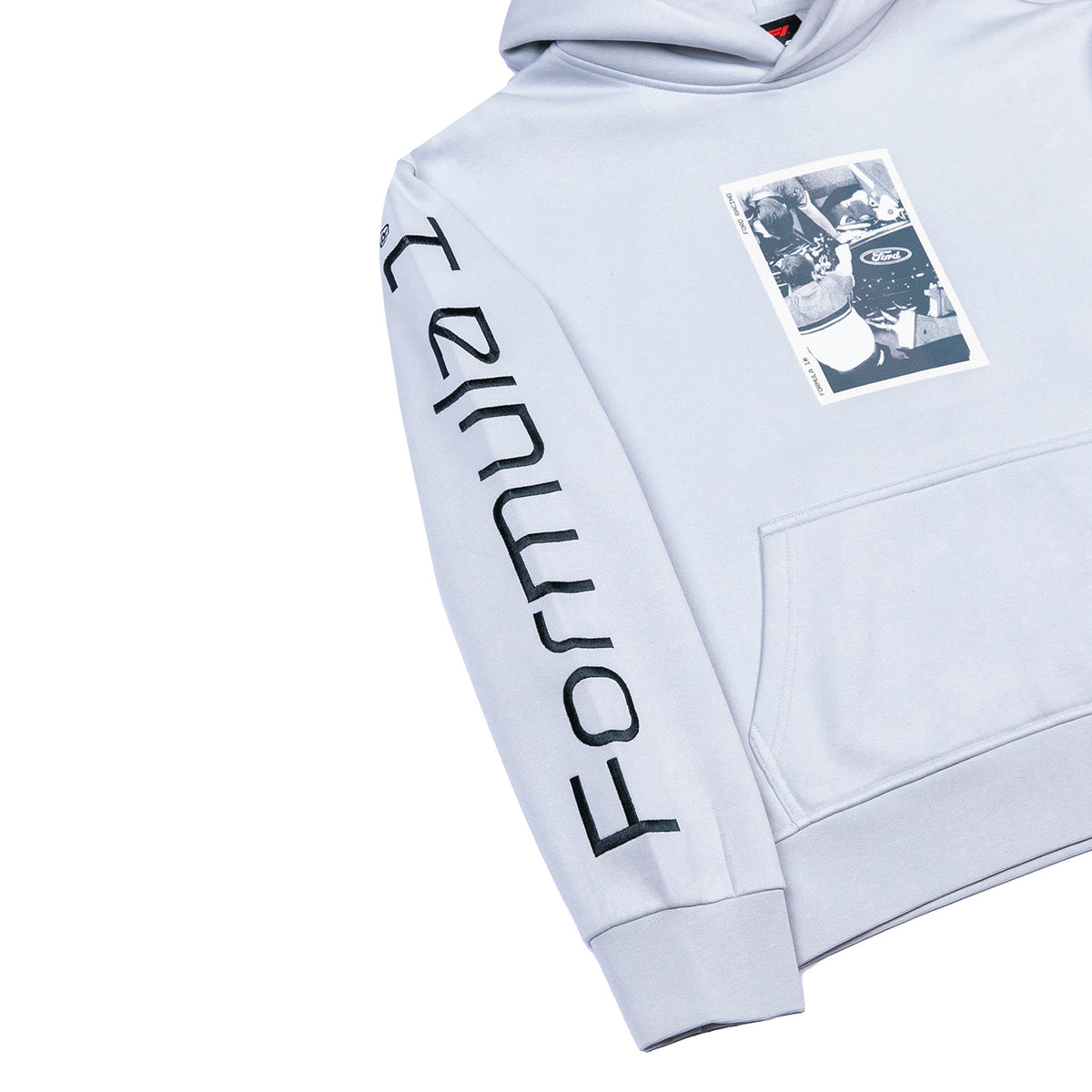 A light gray hooded sweatshirt shown on a white background, featuring a large black 'FORMULA 1' logo printed vertically down one sleeve and a rectangular black-and-white graphic patch on the left chest.
