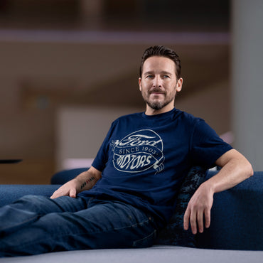 Man wearing a blue Ford t-shirt sitting on a couch.
