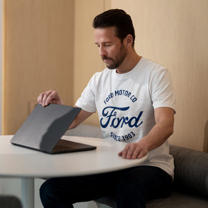 Man wearing a Ford t-shirt sitting at a table with a laptop.