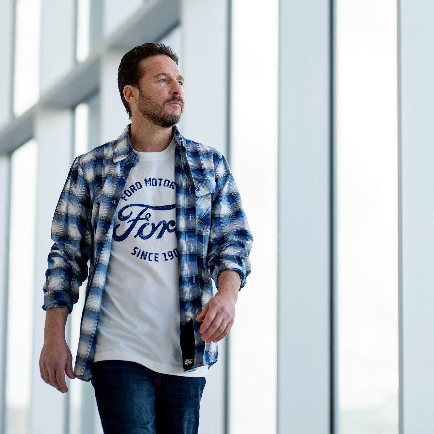 Man wearing a blue and white checkered shirt over a white t-shirt with Ford logo.