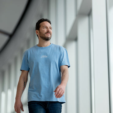 Man wearing a blue t-shirt with a Ford logo, standing in a modern indoor setting.