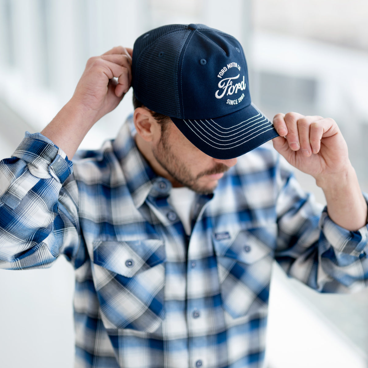 Person wearing a blue cap with branding and a plaid shirt indoors.