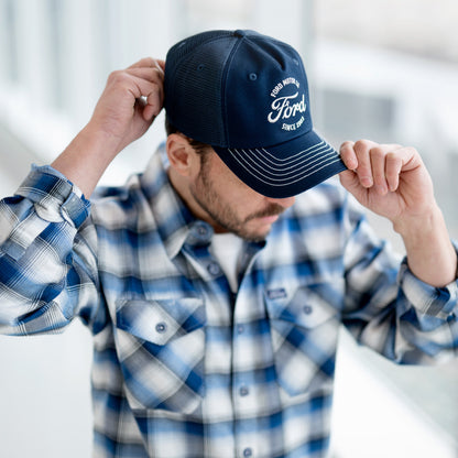 Person wearing a blue cap with branding and a plaid shirt indoors.