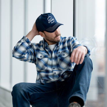 Person wearing a blue and white plaid shirt and cap sitting against a light background