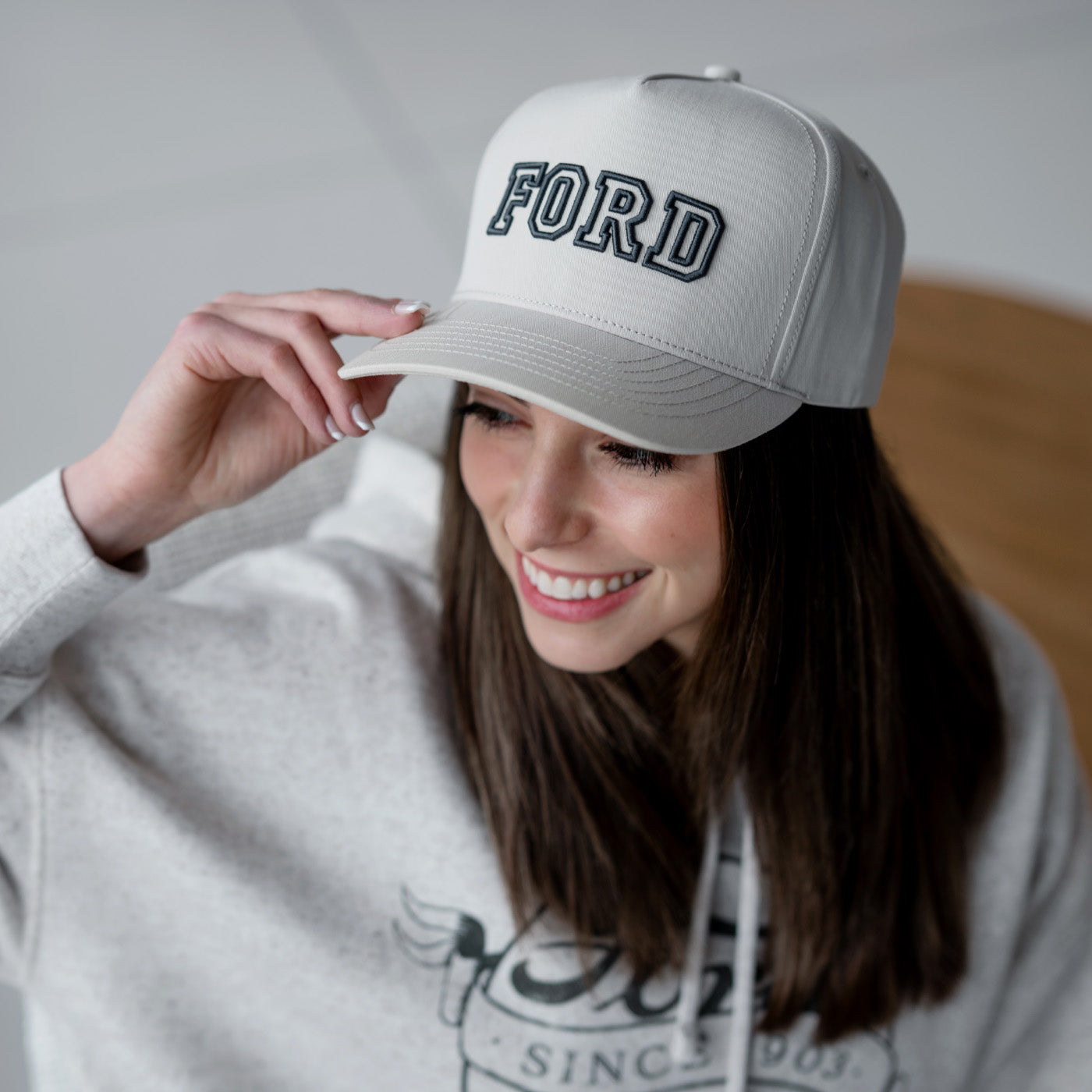 Woman wearing a gray cap with 'FORD' text, smiling against a neutral background