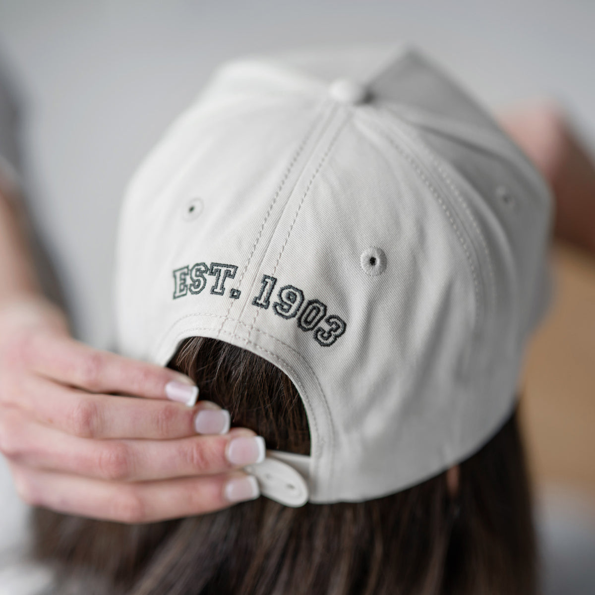 Person wearing a beige cap with 'EST. 1903' text on the back, blurred background