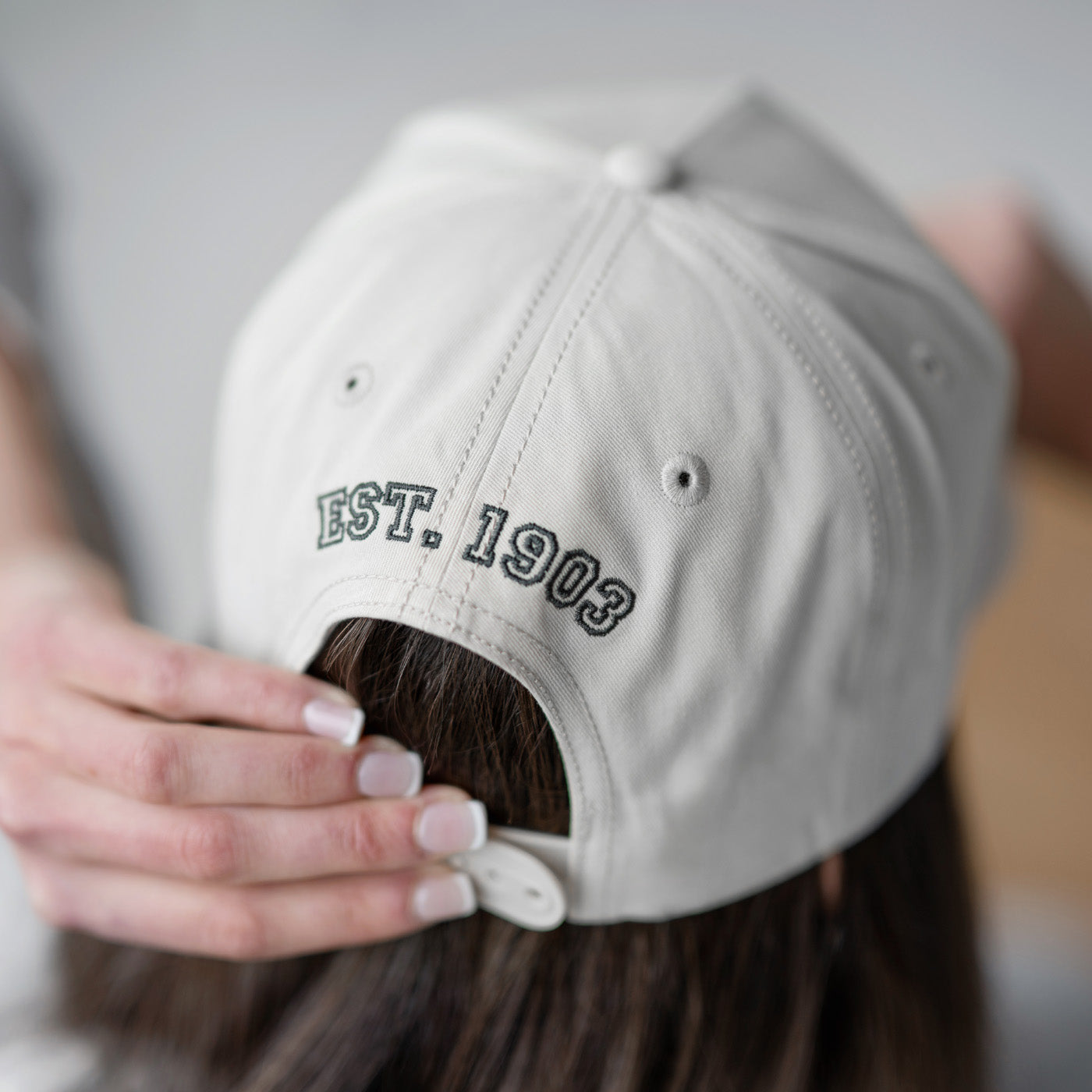 Person wearing a beige cap with 'EST. 1903' text on the back, blurred background