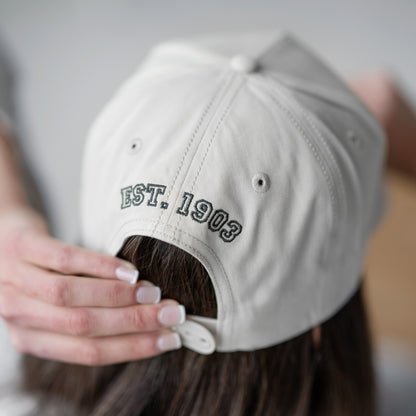 Person wearing a beige cap with 'EST. 1903' text on the back, blurred background