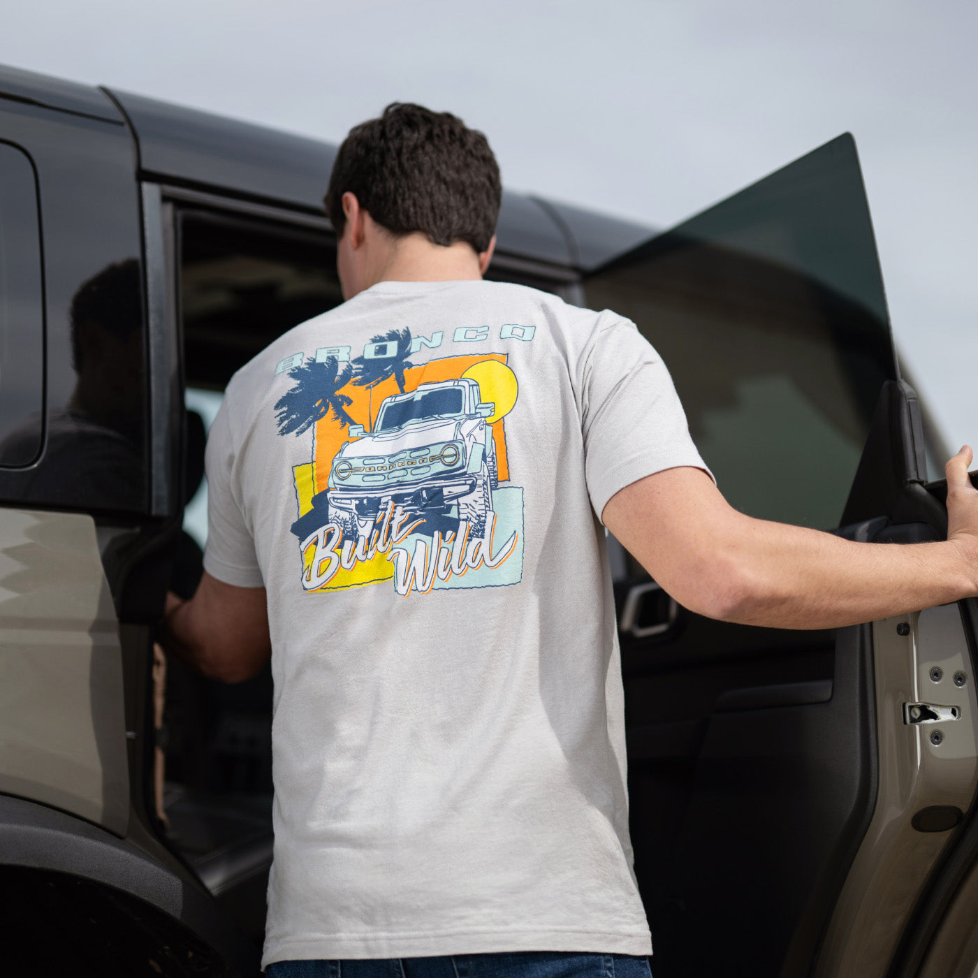 Man opening a car door wearing a t-shirt with a bronco graphic design on the back.