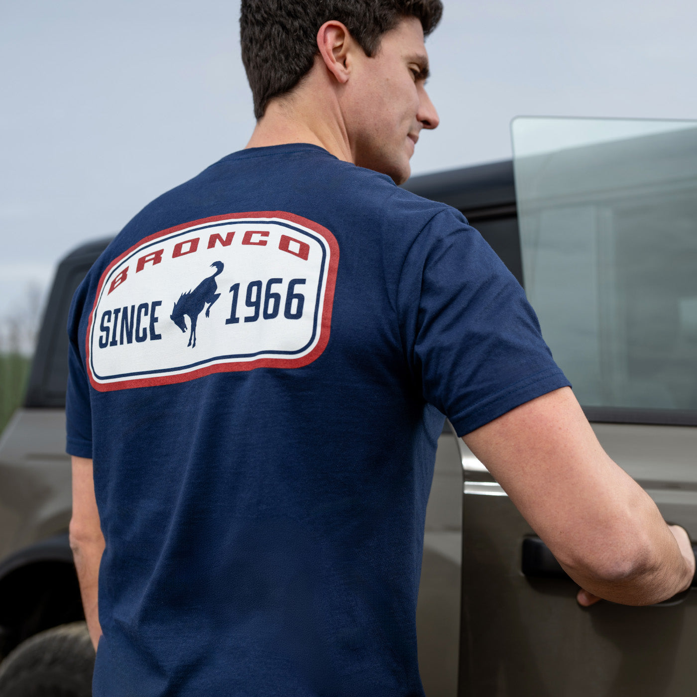 Man wearing a blue t-shirt with 'Bronco Since 1966' logo, standing next to a truck.