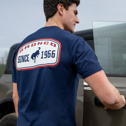 Man wearing a blue t-shirt with 'Bronco Since 1966' logo, standing next to a truck.