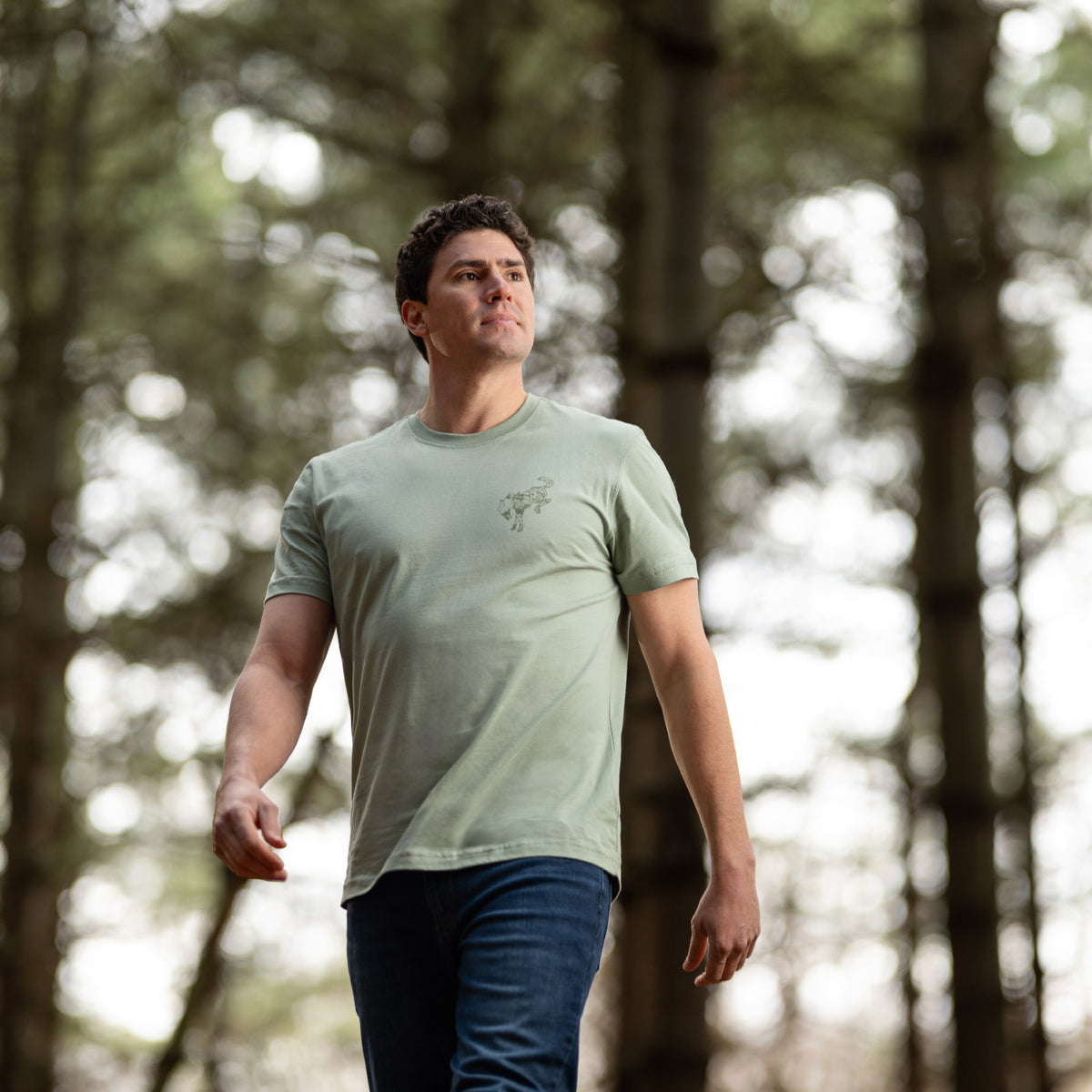 Man walking through a forest wearing a green t-shirt.