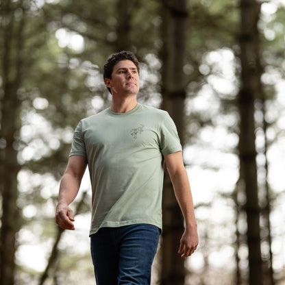 Man walking through a forest wearing a green t-shirt.