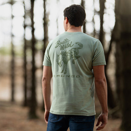 Man wearing a green bronco t-shirt with a graphic design in a forest setting