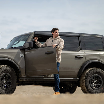 Man opening the door of a gray Bronco SUV in an outdoor setting