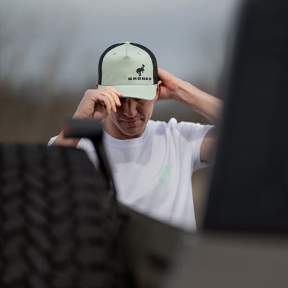 Person wearing a cap with 'BRONCO' branding, standing against a blurred background