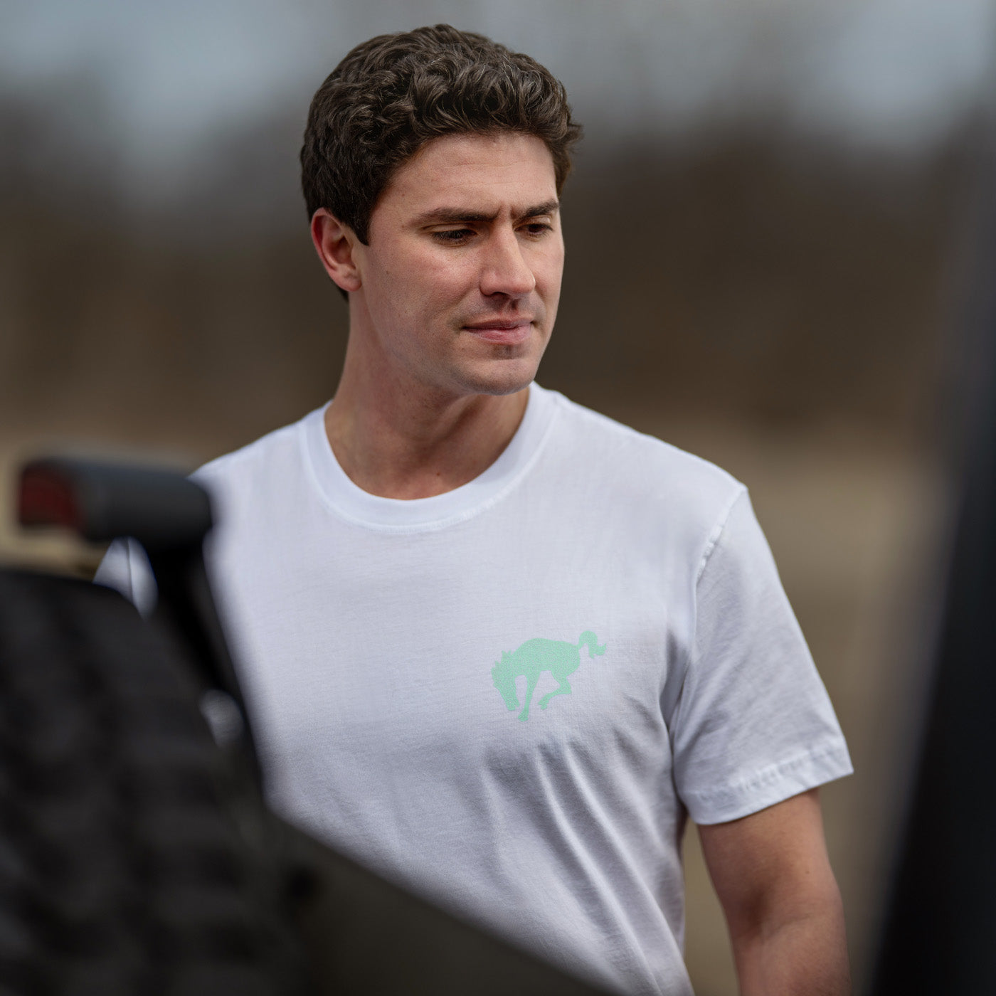 Man wearing a white t-shirt with a green logo, standing outdoors.