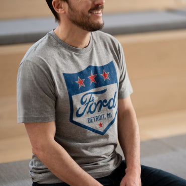 man sitting wearing a gray t-shirt with a ford detroit mi logo 