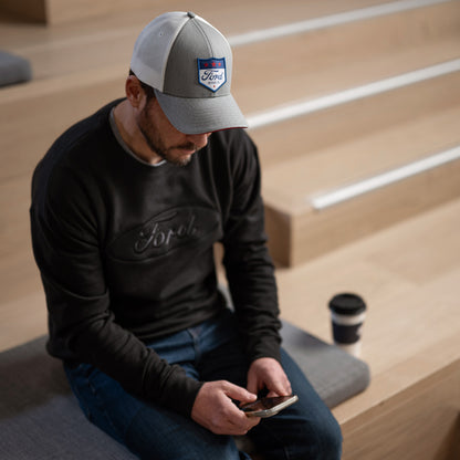 Man wearing a Ford cap and shirt sitting on steps using a phone with a coffee cup beside him.