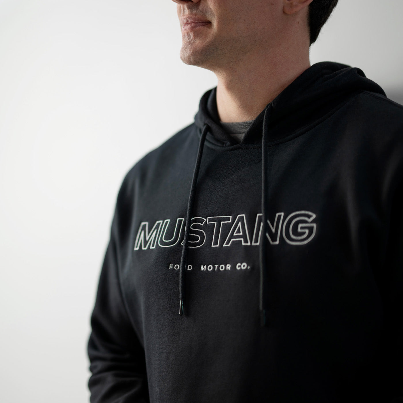 Person wearing a black hoodie with 'Mustang Ford Motor Co.' text on a plain background