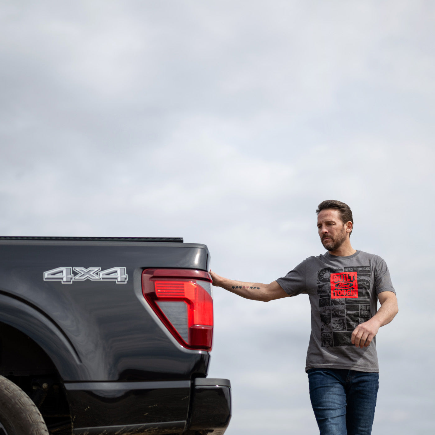 Man standing next to a black pickup truck with '4x4' branding on a cloudy day.