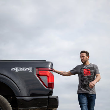 Man standing next to a black pickup truck with '4x4' branding on a cloudy day.