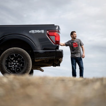 Man standing next to a black Ford F-150 pickup truck with '4x4' branding on a cloudy day.