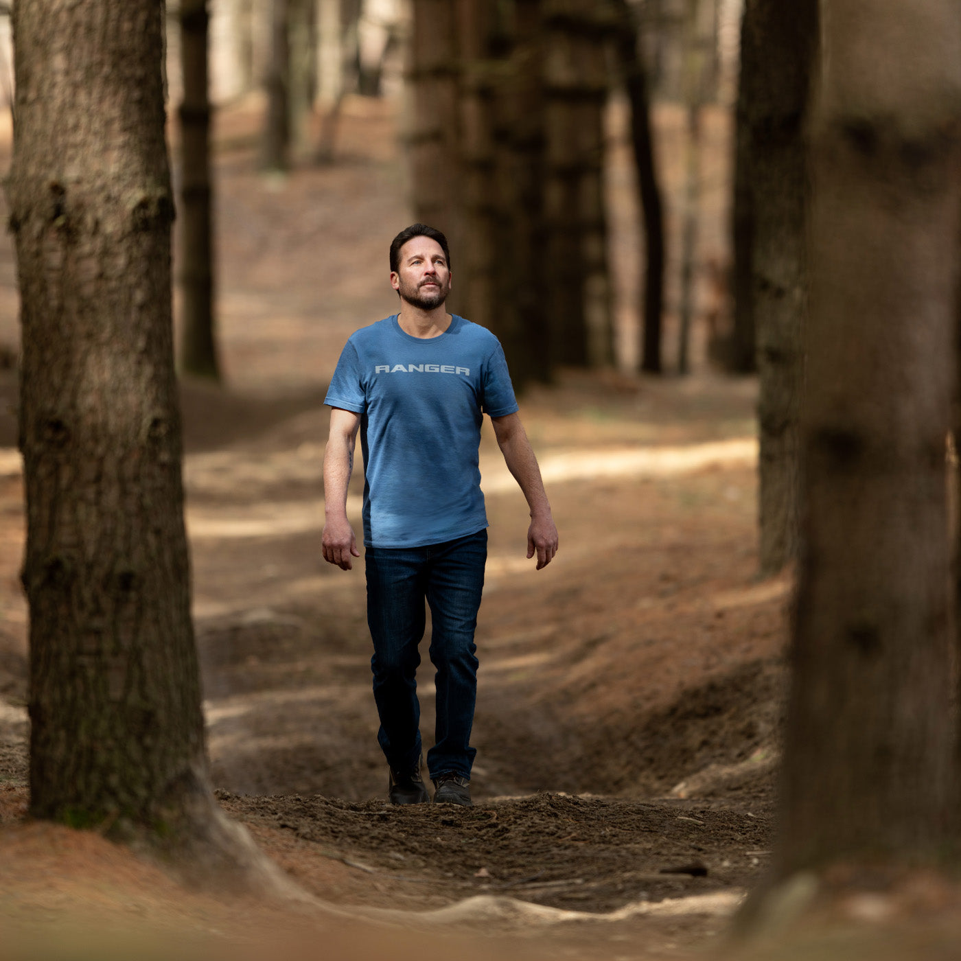 Man walking through a forest wearing a blue t-shirt with 'Ranger' branding.