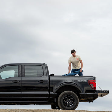 Man standing on a black pickup truck with a neutral background