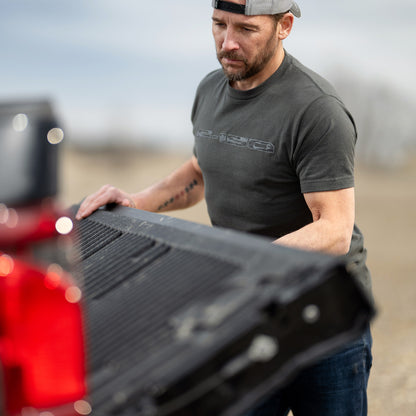 Man adjusting a black truck bed cover outdoors wearing an F-150 shirt
