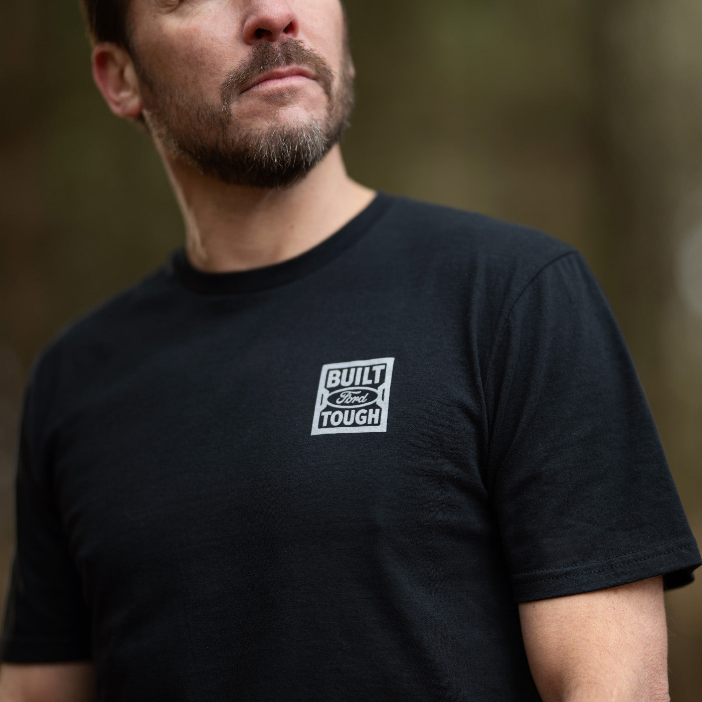 Man wearing a black t-shirt with a logo on a blurred background