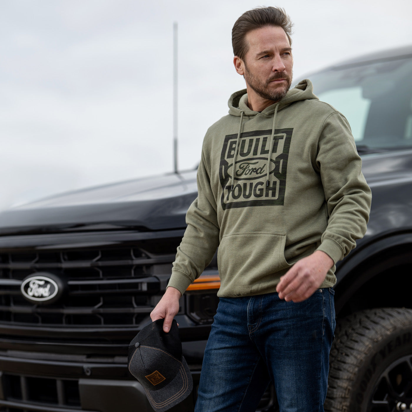 Man wearing a green hoodie with 'Built Ford Tough' text, standing next to a black Ford truck.
