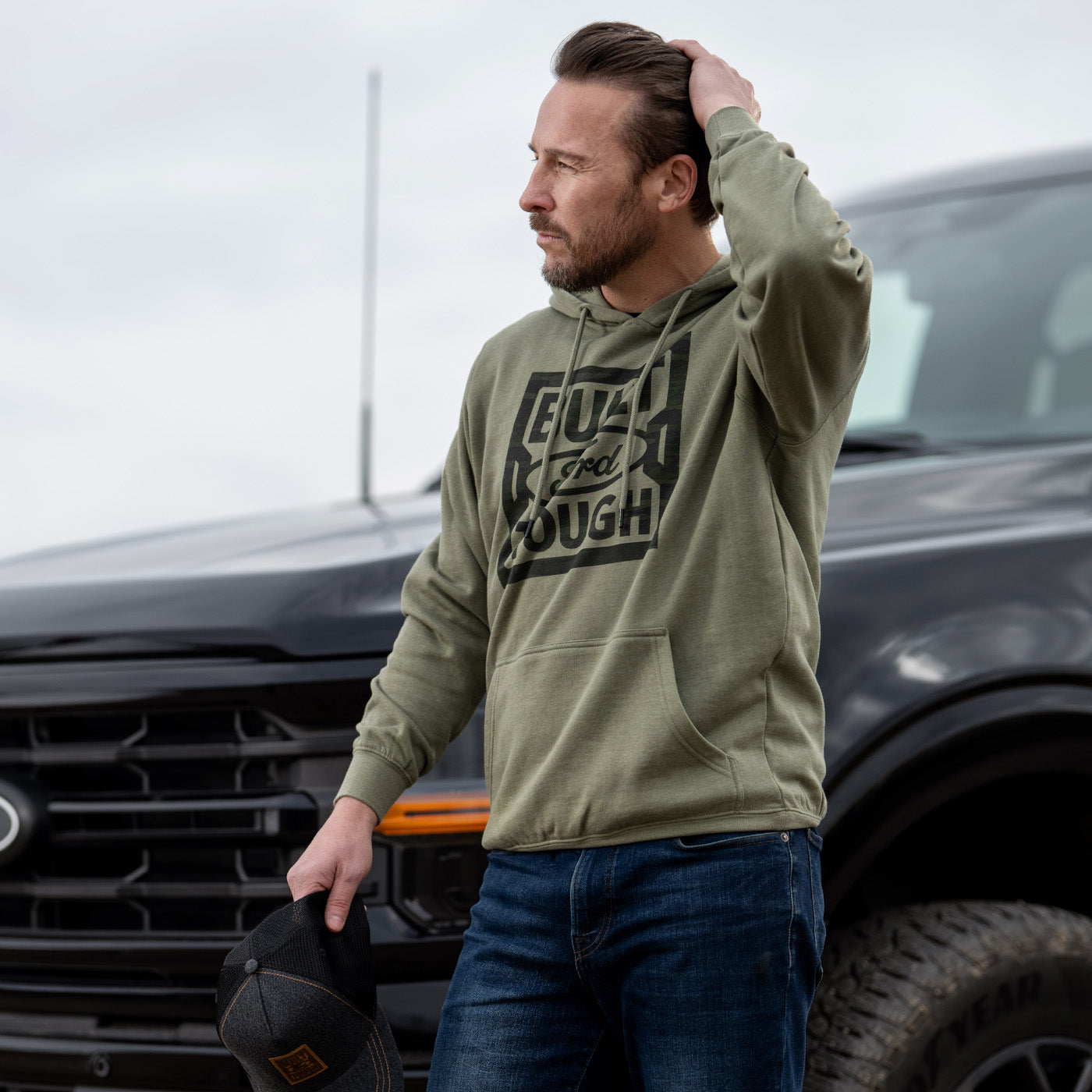 Man wearing a green hoodie with a logo in front of a vehicle