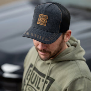 Man wearing a cap and hoodie with Built Ford Tough branding, standing in front of a blurred vehicle.