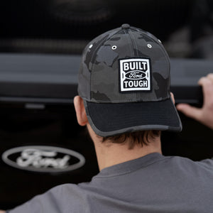 Person wearing a cap with 'Built Ford Tough' logo in front of a Ford vehicle.